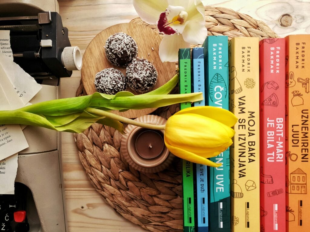 Top view stack of books on table near beautiful yellow tulip and orchid flowers arranged with chocolate truffles placed on wicker placemat